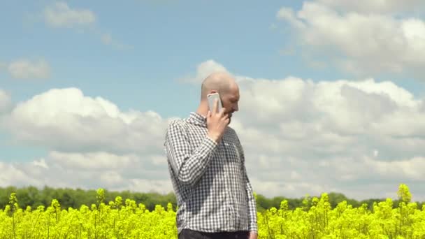 O agricultor está a falar ao telefone no campo de colza. — Vídeo de Stock