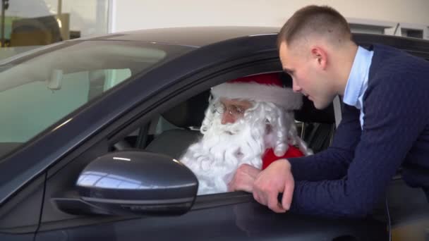 Konsultant w salonie samochodowym prezentujący samochód dla Świętego Mikołaja. Santa kupuje samochód — Wideo stockowe