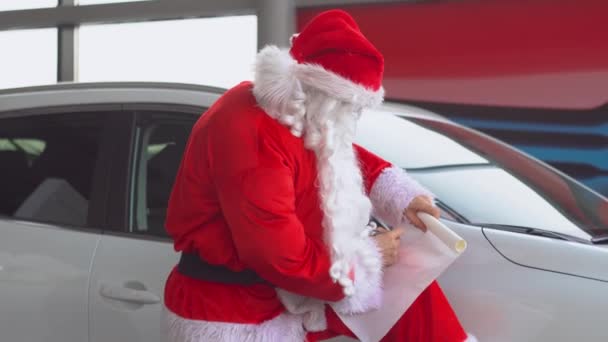 De kerstman bij een autodealer schrijft iets op de lijst. — Stockvideo