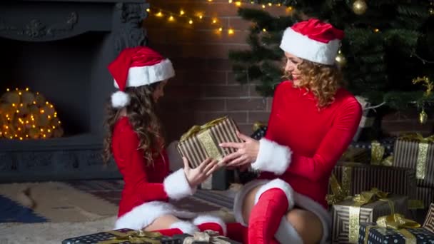Noel kostümlü bir anne ve kız Noel ağacının yanında hediyeler tutuyorlar. — Stok video