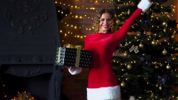 Ung vacker dam i juldräkt håller gåvor nära julgran — Stockvideo