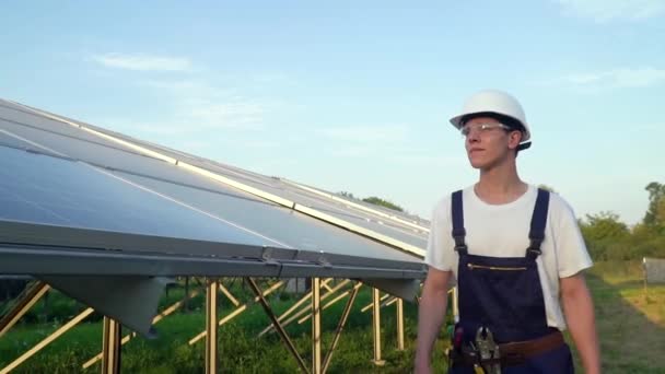 Güneş pili tarlasında yürüyen mühendis güneş enerjisi kurulumundaki panelleri kontrol ediyor. Güneş pilleri geleceğin önemli bir yenilenebilir enerjisi olacak. — Stok video