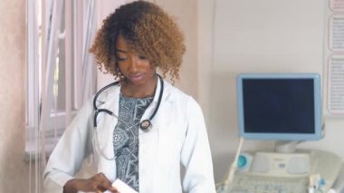 Arka planda ultrason cihazlarıyla hastanede steteskoplu profesyonel Afro-Amerikan kadın doktor portresi. Göğüs kanseri teşhisi.
