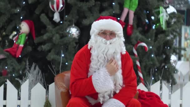 Santa Claus sedí s taškou dárků na nákupním centru a dívá se do kamery — Stock video