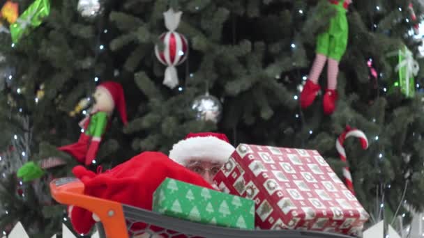 Papá Noel en el emporio escondido detrás de un carrito de compras con regalos — Vídeo de stock