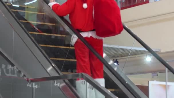 Colpo di Babbo Natale con borsa che si muove sulla scala mobile, sale la scala mobile in un grande centro commerciale — Video Stock