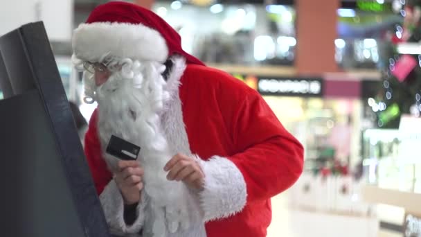 Papai Noel inserir cartão de crédito em bancomat entrar em um pino para receber dinheiro. Papai Noel retirando dinheiro do dispensador de dinheiro em um grande centro comercial — Vídeo de Stock