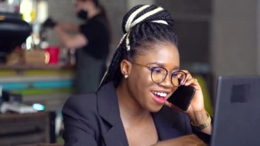 Mutlu Afro-Amerikalı genç kız telefonda konuşuyor ve dizüstü bilgisayar kullanıyor. Zenci kız uzaktan çalışıyor.