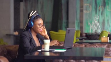 Mutlu Afrikalı Amerikalı genç kadın konferans görüşmesiyle iletişim kuran kulaklık takıyor kafedeki bilgisayara bakıyor. Video sohbet iş görüşmesi ya da uzaktaki dil kursu konsepti