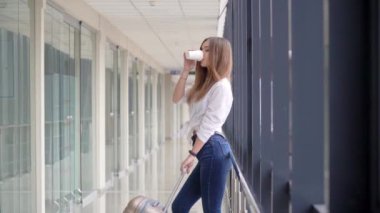 Uçağı beklerken bavul ve kahve taşıyan gezgin kız.