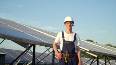 Güneş paneli teknisyenleri güneş panelleri üzerinde çalışıyor. Güneş panellerinin arka planında sınıfını gösteren mutlu genç adam. Gelecek bugündür.