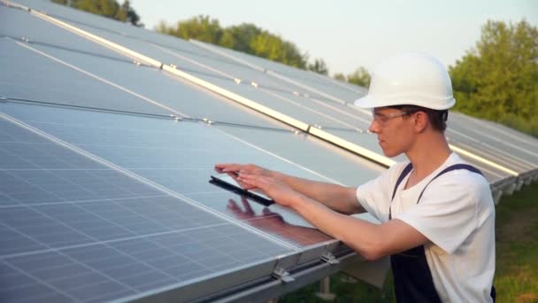 Solpaneltekniker som arbeider med solcellepaneler. Ingeniør i uniform med nettbrett sjekker solcelleets produktivitet. Begrepet grønn energi – stockvideo