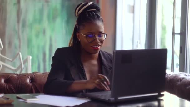 Jovem mulher negra usando computador portátil no café. Profissional do sexo feminino trabalhando com notebook — Vídeo de Stock