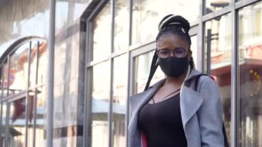 Koronavirüsü önlemek için tıbbi maske takan Afrikalı Amerikalı bir kız ve bir iş merkezindeki kameraya bakıyor. Covid-19 koruması