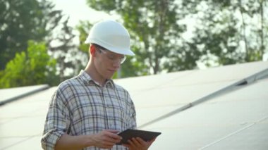 Güneş paneli teknisyenleri güneş panelleri üzerinde çalışıyor. Tabletli mühendis güneş panelinin verimliliğini kontrol ediyor. Fotovoltaik panel