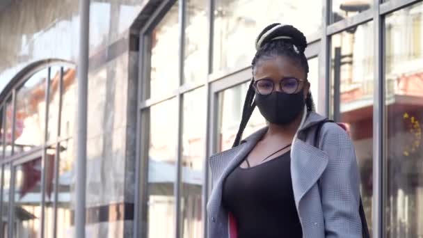 Afro-Amerikaans meisje met een medisch masker voor de preventie van het coronavirus en kijkend naar de camera in een business center. Covid-19 bescherming — Stockvideo
