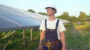 Güneş pili tarlasında yürüyen teknisyen güneş enerjisi kurulumundaki panelleri kontrol ediyor. Kavramsal yenilenebilir enerji