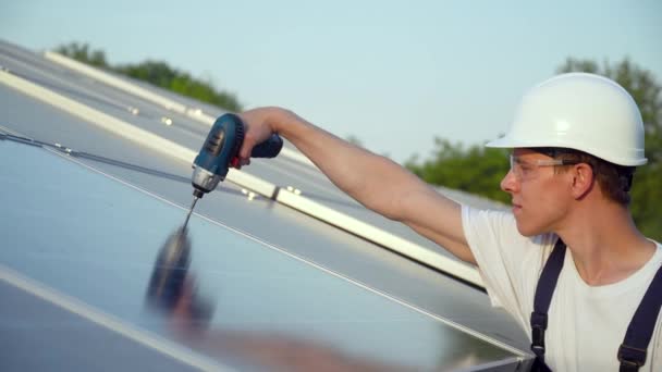 Motor joven instalando nuevas baterías soleadas. Trabajador en uniforme y hardhat instalando paneles fotovoltaicos en una granja solar — Vídeo de stock