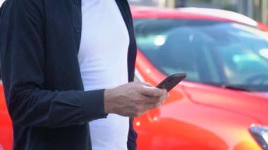 Modern arabanın yanında akıllı telefon kullanan kendine güvenen bir adam. Akıllı telefonunu kullanan genç iş adamının yakın çekimi.