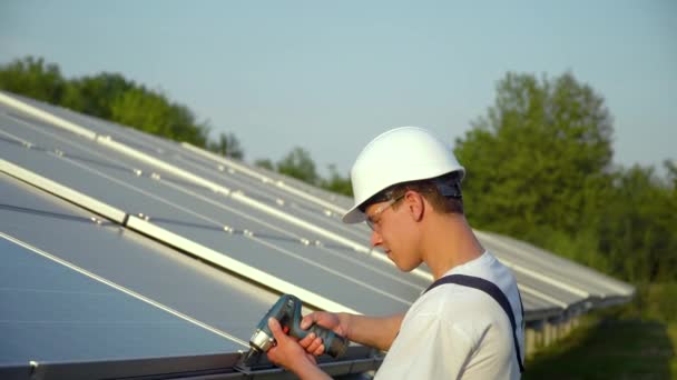 Giovane enginneer l'installazione di nuove batterie solari. Lavoratore in uniforme e hardhat che installa pannelli fotovoltaici in una fattoria solare. Concetto di energie rinnovabili — Video Stock