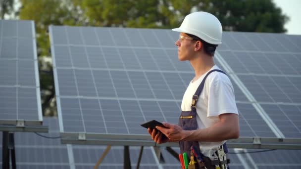 Tecnico dei pannelli solari che lavora con i pannelli solari. Ingegnere in uniforme con tablet controlla la produttività dei pannelli solari. Il futuro è oggi — Video Stock