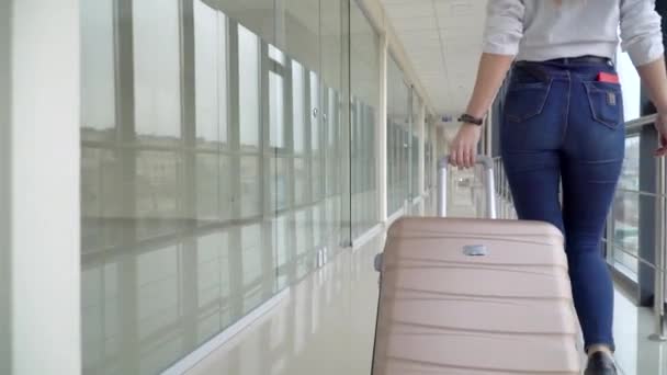Gadis pelancong berjalan pergi dengan bagasi sambil menunggu untuk transportasi. Gadis muda menarik koper di terminal bandara modern. Perjalanan setelah karantina — Stok Video