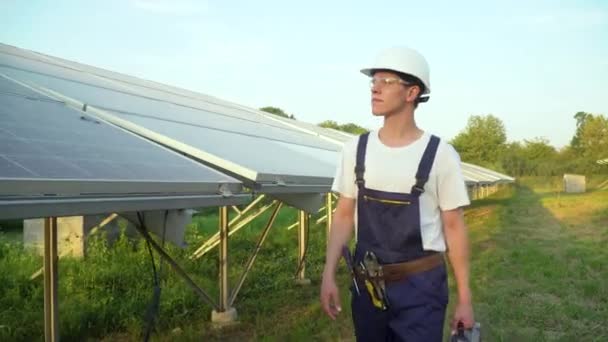 Ingeniero caminando en granja de células solares a través del campo de paneles solares comprobando los paneles en la instalación de energía solar. Las células solares serán una importante energía renovable del futuro — Vídeos de Stock
