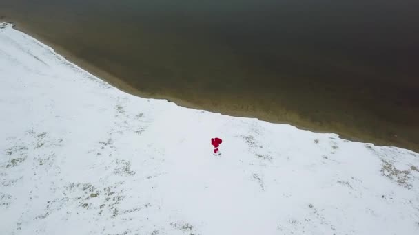 Zmęczony Święty Mikołaj idzie z torbą prezentów wzdłuż śnieżnego arktycznego brzegu oceanu. Widok z góry — Wideo stockowe