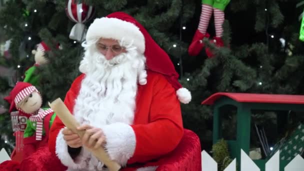 Santa Claus sedí s pytlíkem dárků v supermarketu a píše něco do seznamu — Stock video
