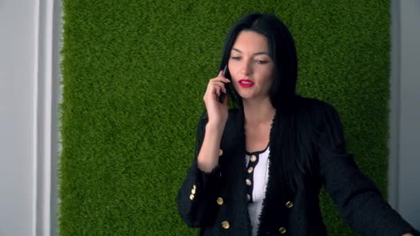 Joven mujer de negocios hablando por teléfono móvil en la oficina con fondo verde herboso. Entrevista de trabajo online — Vídeos de Stock