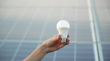 Güneş panelinin arka planında lambayı tutan bir kadının yakın çekimi. Yeşil enerji kavramı