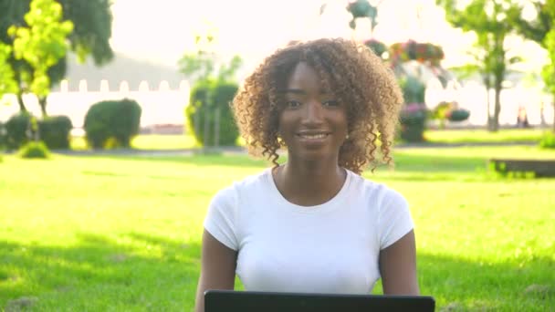 Vacker ung afrikansk amerikansk kvinna söt ansikte med laptop tittar på kameran poserar ensam i parken, glad tusenårig afrikansk etnicitet flicka student professionell närbild framsidan porträtt — Stockvideo