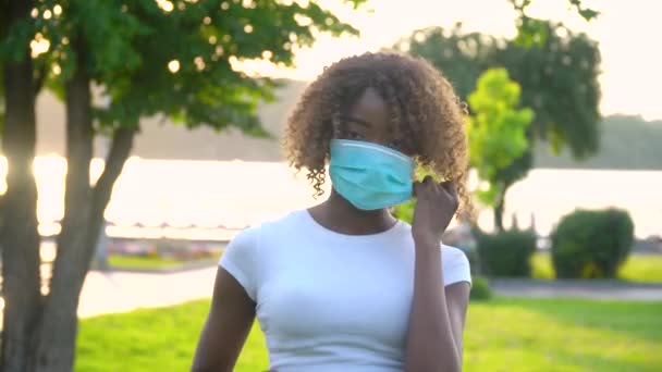 Fata afro-americană îndepărtează o mască medicală în parc. Sfârșitul carantinei — Videoclip de stoc