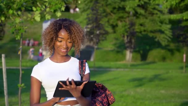 대학 공원에서 태블릿을 사용하고 있는 젊은 아프리카계 미국 여성 학생 — 비디오