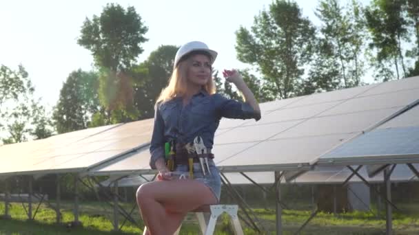 Eine Ingenieurin mit weißem Helm blickt in die Kamera und schaut auf das Solarkraftwerk. Alternatives Energiekonzept — Stockvideo
