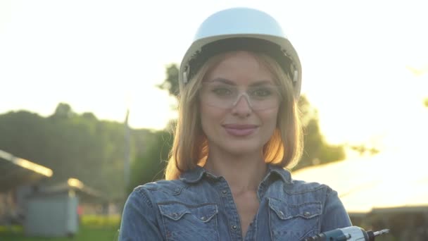 Engenheira mulher em um capacete branco com chave de fenda olhando para a câmera está na central de energia solar. O conceito de energia verde — Vídeo de Stock