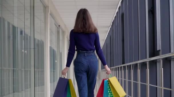 Fiatal lány színes bevásárlószatyrokkal sétál a bevásárlóközpontban. Biztonságos vásárlás — Stock videók