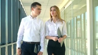 Modern cam ofis koridorunda yürüyen iş çifti. İş adamı ve sekreteri ofis merkezinin pencerelerinin yanında yürüyorlar.
