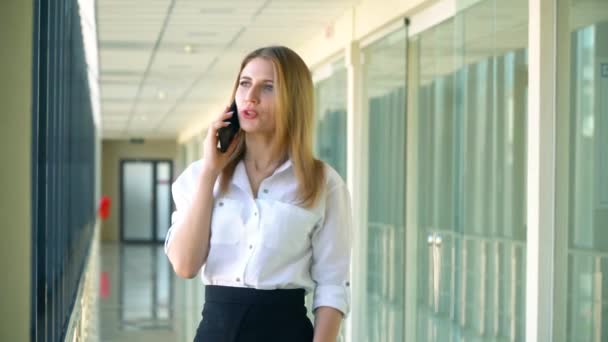 Jonge zakenvrouw staat in zijn kantoor en praat aan de telefoon over de volgende grote zakelijke deal, kijkend uit het raam — Stockvideo