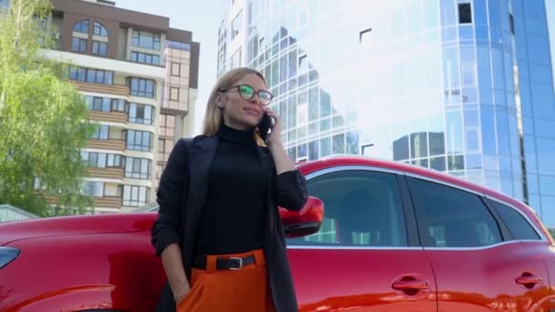 Erfolgreiche Geschäftsfrau steht in der Nähe eines roten Autos, während sie in der Nähe eines Geschäftszentrums mit dem Smartphone spricht — Stockvideo