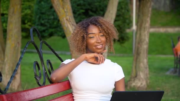 아름다운 젊은 흑인 여성예쁜 얼굴을 하고 대학 공원에서 홀로 포즈를 취하고 있는 카메라를 보고 있는 노트북을 보고 행복 해 하고 있습니다. — 비디오
