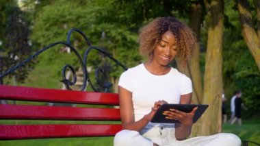 Üniversite parkında tablet kullanan Afrikalı Amerikalı genç bir kadın.