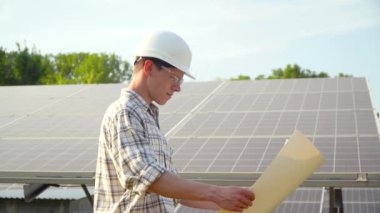 Genç makinist yeni güneşli bataryalar kuruyor. Güneş çiftliğine fotovoltaik paneller monte eden sabit kasklı bir işçi