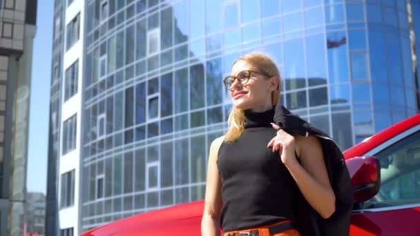 Attraktiv affärskvinna med långt hår nära lyx bil tittar på kameran på en byggnad bakgrund — Stockvideo
