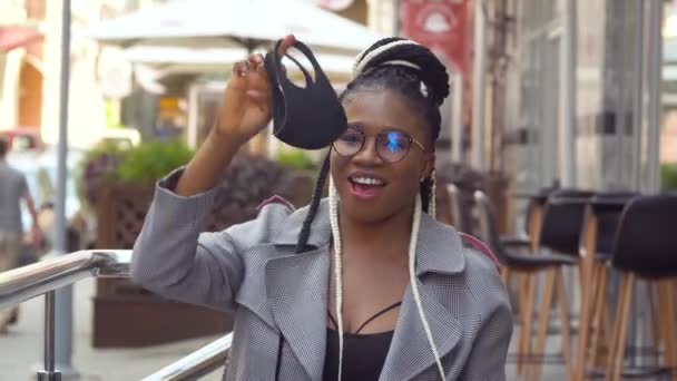 Komik siyah kız sokak kafesinde tıbbi maskesini çıkarıyor. Sosyal mesafe kavramı. Karantinanın sonu — Stok video