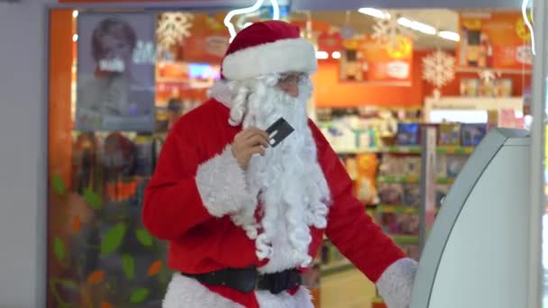 Santa Claus con una tarjeta de crédito cerca de un cajero automático en un gran centro comercial — Vídeo de stock