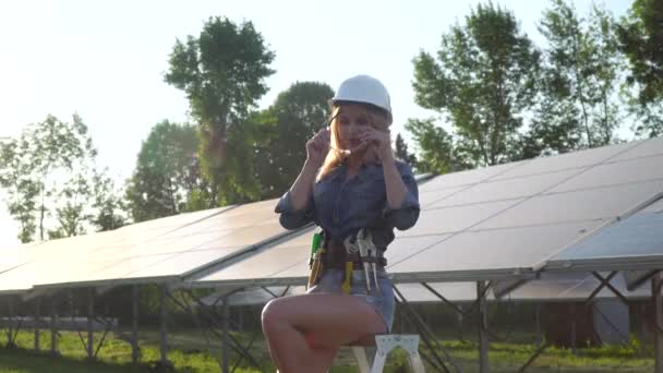 Eine Ingenieurin mit weißem Helm setzt eine Brille auf und steht am Solarkraftwerk. Alternatives Energiekonzept — Stockvideo