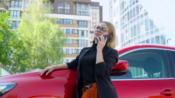 Framgångsrik kvinna står nära en röd bil när du talar på smartphone nära business center — Stockvideo