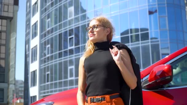 Привлекательная стильная женщина с длинными волосами возле роскошного автомобиля на заднем плане здания — стоковое видео