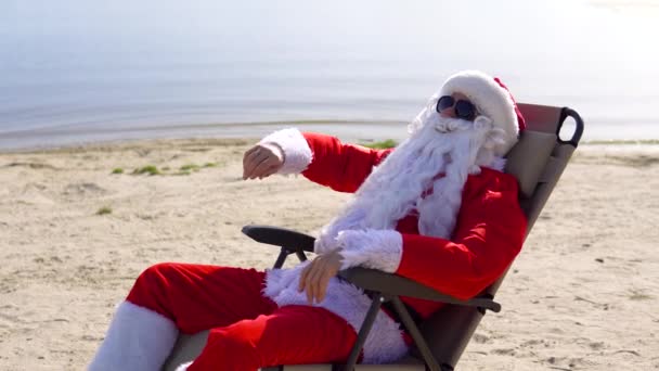 圣诞老人戴着太阳镜，躺在沙滩上晒太阳，一边喝着鸡尾酒 — 图库视频影像